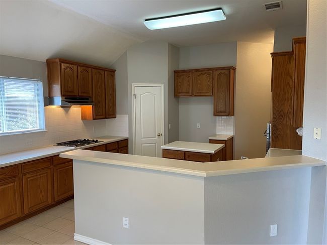 Kitchen featuring brown cabinets, range hood, tasteful backsplash, lofted ceiling, and light countertops | Image 9