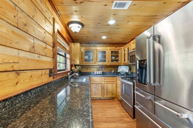 This cozy kitchen features warm wood paneling, granite countertops, and stainless steel appliances, creating a rustic yet modern feel. The natural light from the window enhances the inviting atmosphere. | Image 50