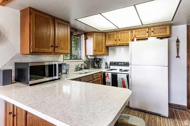 Kitchen with white appliances, a peninsula, light countertops, brown cabinetry, and a textured ceiling | Image 19