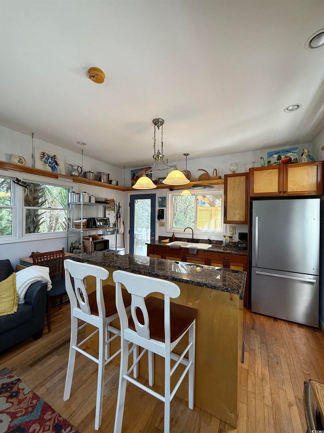 Kitchen with freestanding refrigerator, a kitchen island, light wood-style floors, a sink, and hanging light fixtures | Image 10