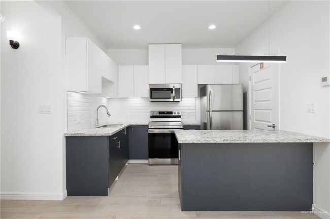 Kitchen with appliances with stainless steel finishes, light stone counters, backsplash, white cabinetry, and recessed lighting | Image 5