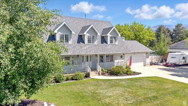 Cape cod home with covered porch, a garage, driveway, a front yard, and roof with shingles | Image 34