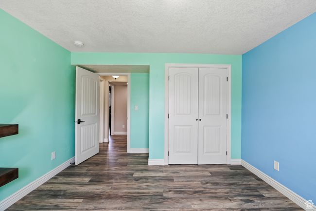 Unfurnished bedroom featuring a textured ceiling, baseboards, dark wood-style floors, and a closet | Image 21