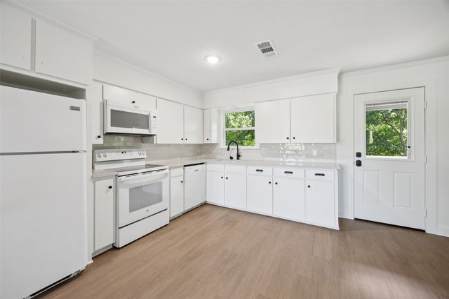 Kitchen with white appliances, light countertops, light wood finished floors, backsplash, and ornamental molding | Image 7