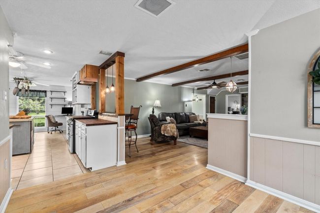 This photo showcases a spacious open-concept living area with a modern kitchen featuring wood accents and pendant lighting. The room includes a cozy seating area with a large sectional sofa, exposed beams, and ample natural light, creating a warm and inviting atmosphere. | Image 13