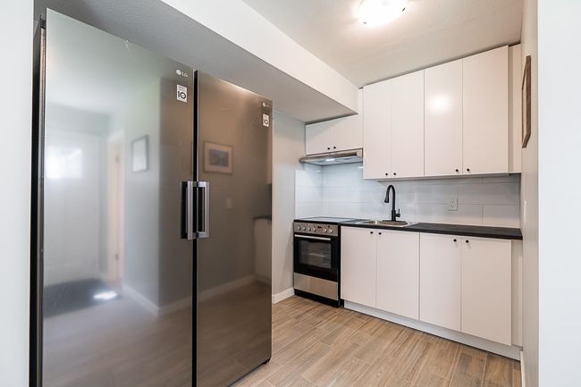 Kitchen featuring appliances with stainless steel finishes, a sink, dark countertops, under cabinet range hood, and light wood-style floors | Image 27