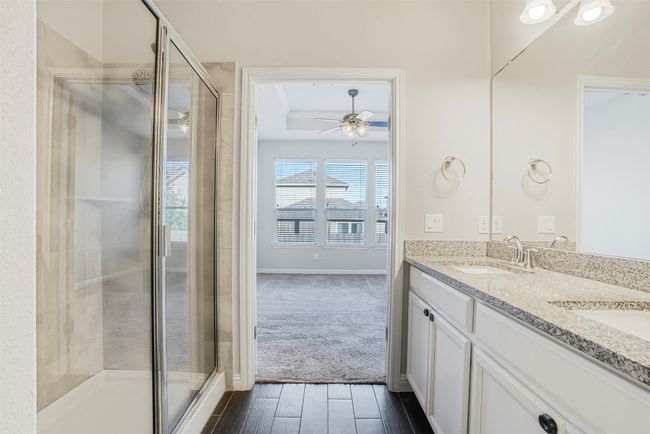 Bathroom featuring a tray ceiling, double vanity, a stall shower, wood finished floors, and a ceiling fan | Image 23