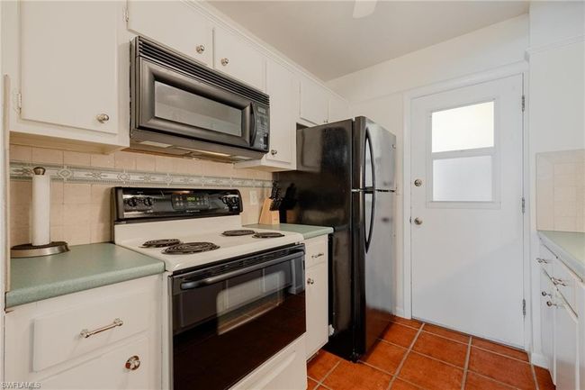 Kitchen with white range with electric cooktop, tile floors, white cabinets, backsplash, and stainless steel refrigerator | Image 17