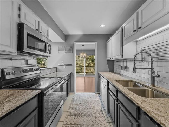 Kitchen with sink, stainless steel appliances, light stone countertops, white cabinets, and decorative light fixtures | Image 11