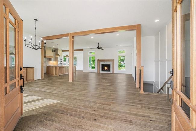 Unfurnished living room with light wood finished floors, a chandelier, a lit fireplace, ceiling fan, and recessed lighting | Image 11