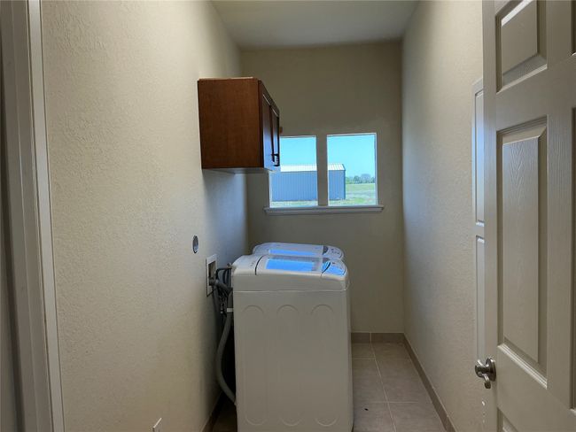 Laundry room featuring light tile patterned flooring, washer / dryer, cabinet space, a textured wall, and baseboards | Image 19