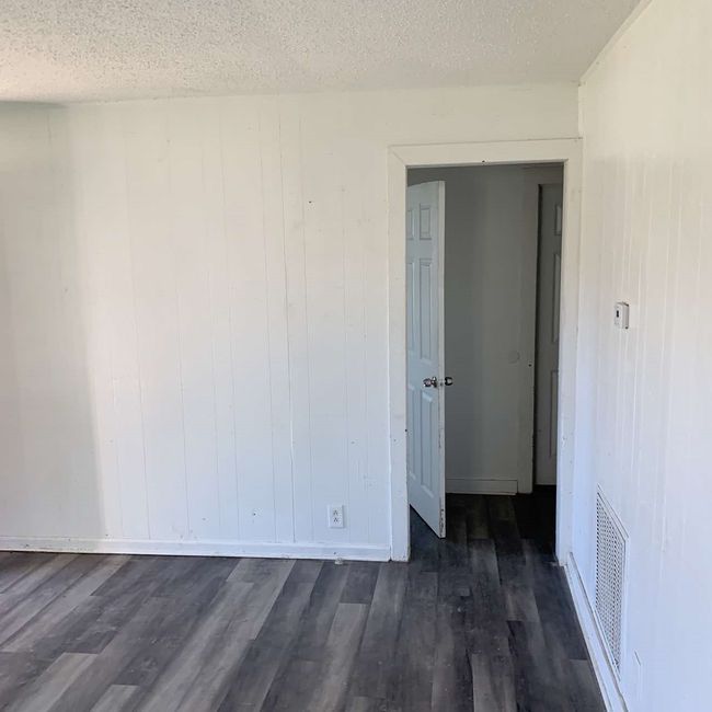 Empty room with dark wood-style flooring, a textured ceiling, and wooden walls | Image 4