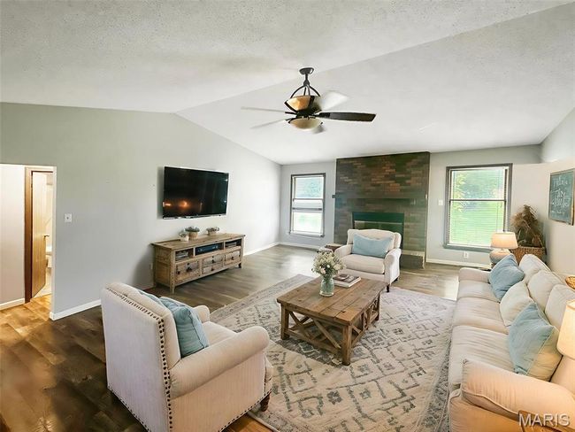Living room with a ceiling fan, lofted ceiling, wood finished floors, a textured ceiling, and a large fireplace | Image 4