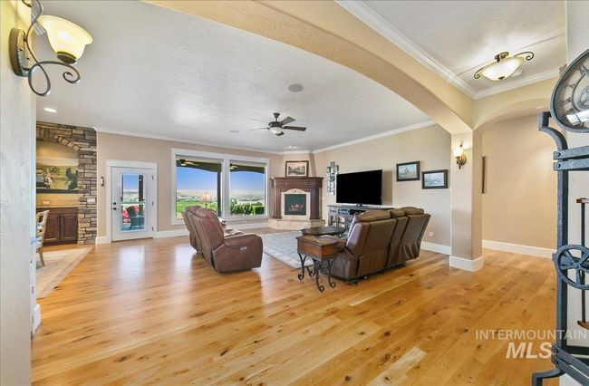 Living area with a lit fireplace, light wood finished floors, a ceiling fan, arched walkways, and a textured ceiling | Image 5