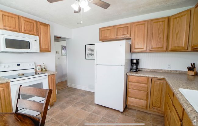 Kitchen with white appliances, ceiling fan, light countertops, stone finish floors, and a sink | Image 6