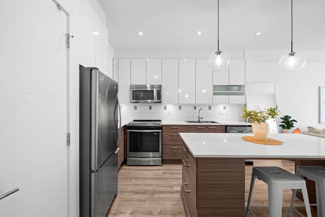 Kitchen with a sink, a breakfast bar, white cabinetry, modern cabinets, and appliances with stainless steel finishes | Image 11