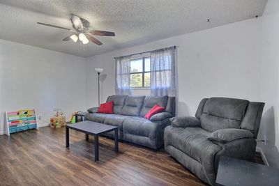 Living room with a textured ceiling, dark wood-type flooring, and ceiling fan | Image 2