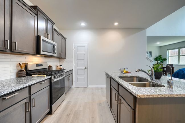 Kitchen with stainless steel appliances, a sink, light wood finished floors, light stone counters, and decorative backsplash | Image 12