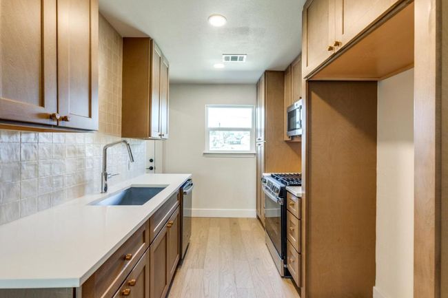 Kitchen with light wood finished floors, tasteful backsplash, visible vents, appliances with stainless steel finishes, and a sink | Image 15