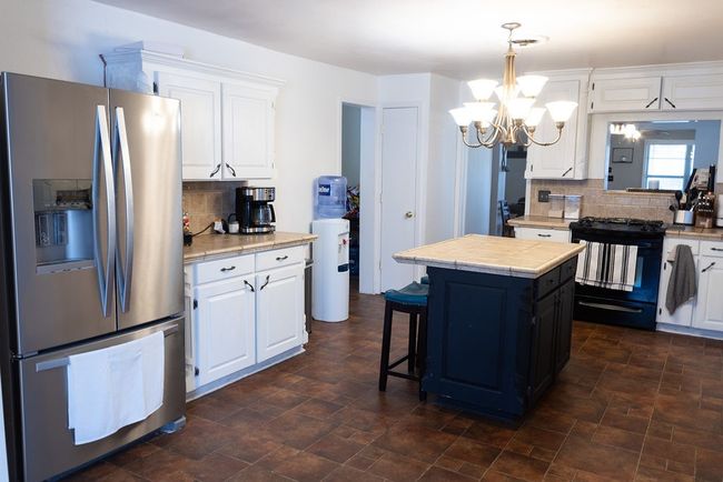 Kitchen featuring stainless steel refrigerator with ice dispenser, black gas stove, backsplash, and a chandelier | Image 8