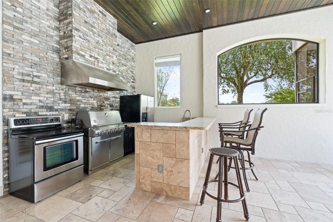 This fully equipped outdoor kitchen features a premium grill, range, full-size refrigerator, and granite bar—ideal for effortless entertaining in style. | Image 4
