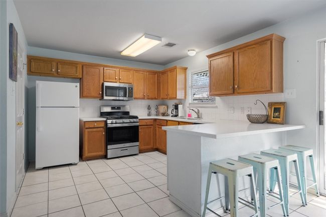 Kitchen with tasteful backsplash, visible vents, appliances with stainless steel finishes, a sink, and a peninsula | Image 11