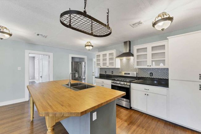 Kitchen with butcher block countertops, visible vents, wall chimney exhaust hood, appliances with stainless steel finishes, and a sink | Image 5