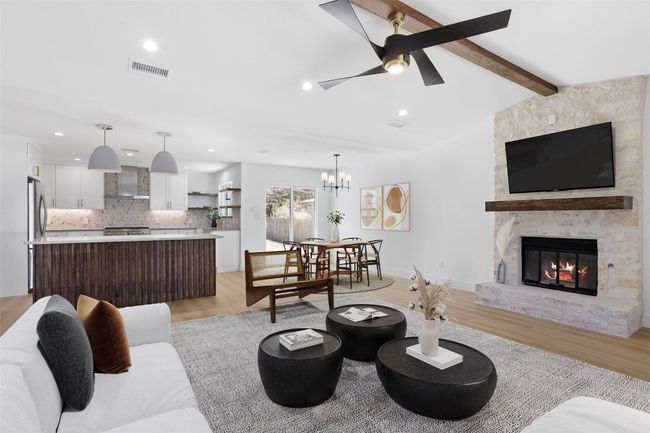 Living room featuring Minka Aire ceiling fan, brand new flooring, vaulted ceiling with a beam, and a stone fireplace | Image 4