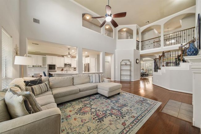 A view of the living room with the kitchen & breakfast room in the background. Notice the wrought iron balcony and arched openings overlooking the living area from the second level of the home. | Image 12