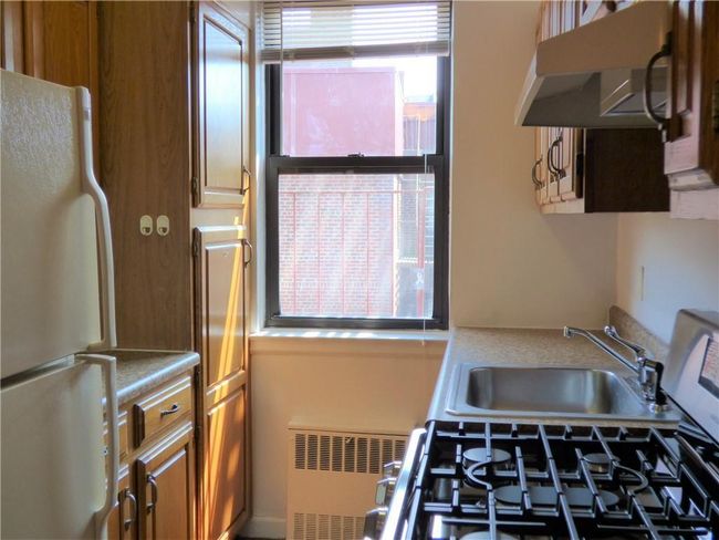 Kitchen with exhaust hood, light countertops, freestanding refrigerator, brown cabinets, and radiator | Image 6