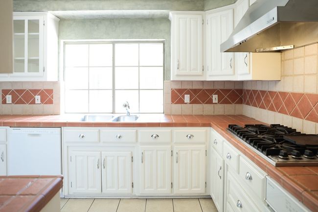 Kitchen with under cabinet range hood, dishwasher, tile counters, stainless steel gas stovetop, and white cabinetry | Image 22