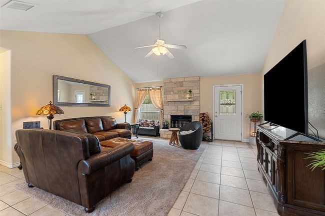 Living area featuring lofted ceiling, light tile patterned floors, ceiling fan, a stone fireplace, and baseboards | Image 10