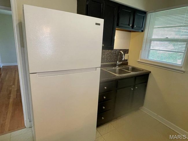 Kitchen featuring dark cabinetry, a sink, freestanding refrigerator, baseboards, and decorative backsplash | Image 11