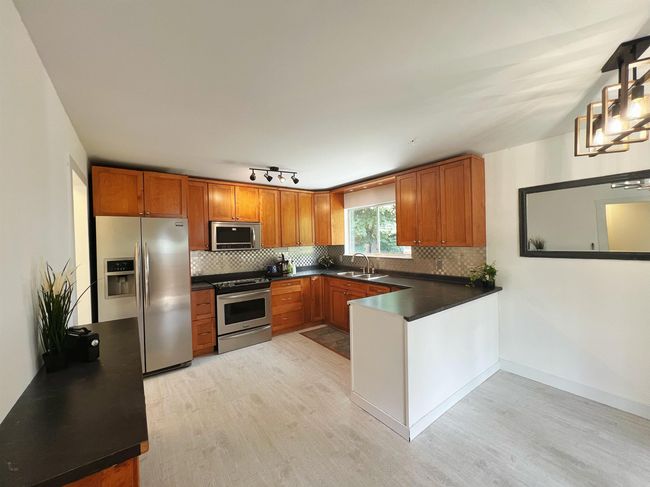 Kitchen featuring appliances with stainless steel finishes, light wood finished floors, a peninsula, dark countertops, and tasteful backsplash | Image 4