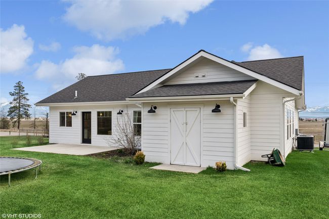 Rear view of property featuring a trampoline, roof with shingles, a patio area, central AC unit, and a yard | Image 39