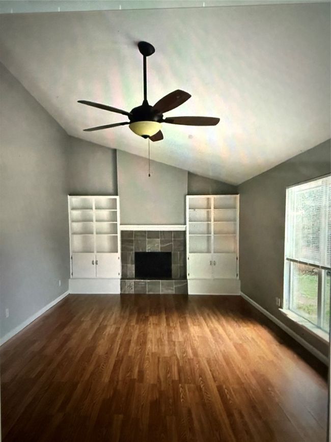 Unfurnished living room featuring lofted ceiling, dark wood-style floors, a ceiling fan, and a fireplace | Image 6