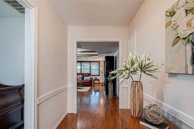 A welcoming hallway with elegant wood flooring leading into a bright living area. The space features tasteful decor and opens into the family room with large windows that provide natural light. | Image 4