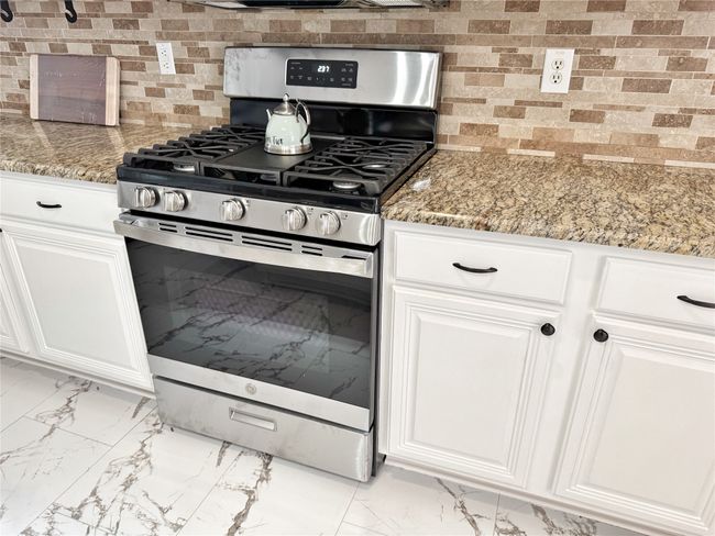 Kitchen with stainless steel gas range, light marble finish floors, backsplash, white cabinetry, and light stone counters | Image 10