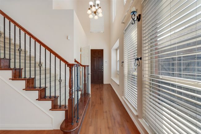 Entrance foyer with a towering ceiling, wood finished floors, a chandelier, and stairway | Image 6