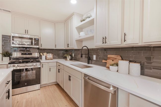 Kitchen with stainless steel appliances, open shelves, backsplash, and white cabinets | Image 11