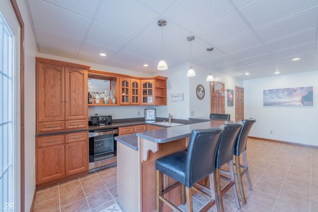 Lower level bar/kitchen with open shelves, dark countertops, brown cabinetry, and a breakfast bar area | Image 17