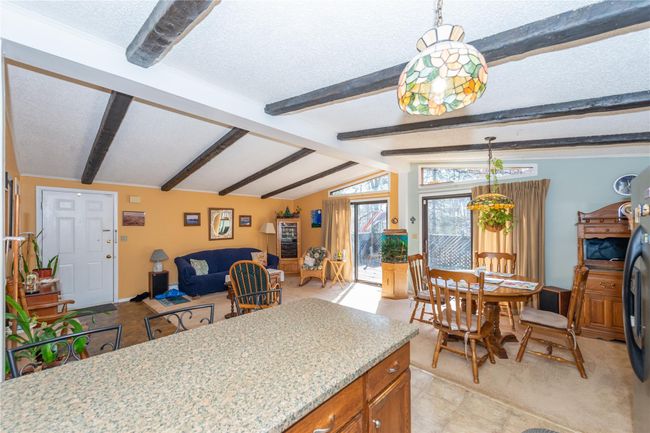 Kitchen with brown cabinets, open floor plan, vaulted ceiling with beams, light stone countertops, and a textured ceiling | Image 8
