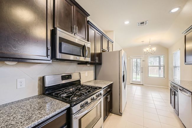 Kitchen with stainless steel appliances, dark brown cabinetry, a chandelier, light stone countertops, and decorative backsplash | Image 10