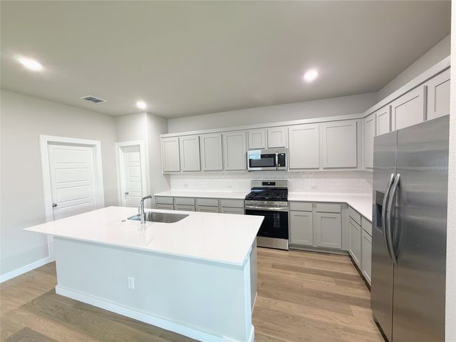 Kitchen featuring appliances with stainless steel finishes, a sink, gray cabinets, light wood-type flooring, and tasteful backsplash | Image 14
