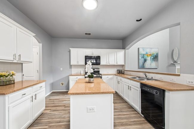 Kitchen with arched walkways, light wood-style flooring, a sink, and black appliances | Image 13