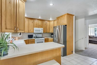 Kitchen featuring light carpet, white appliances, kitchen peninsula, and sink | Image 3