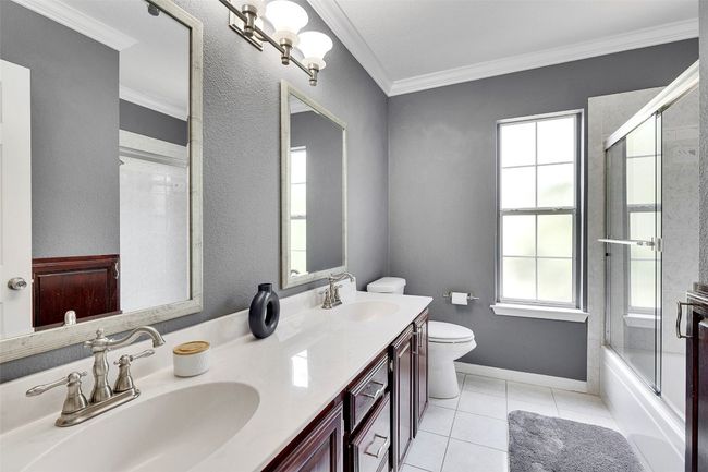 Full bathroom featuring toilet, double vanity, ornamental molding, enclosed tub / shower combo, and tile patterned floors | Image 26