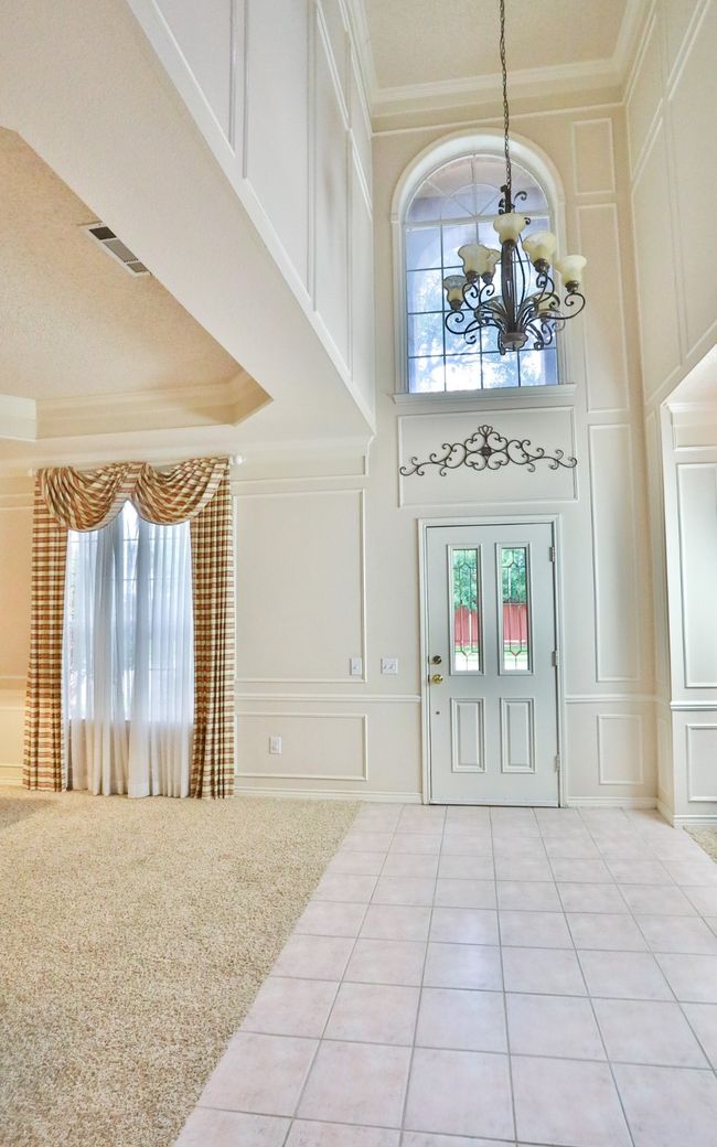 Entryway featuring a decorative wall, a chandelier, plenty of natural light, crown molding, and a high ceiling | Image 14