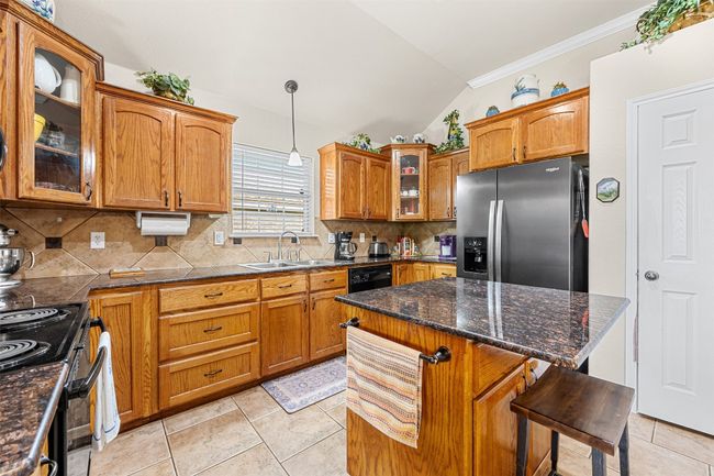 Kitchen featuring black appliances, a sink, vaulted ceiling, brown cabinets, and tasteful backsplash | Image 13