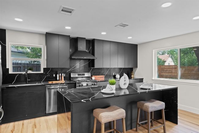Kitchen featuring wall chimney exhaust hood, appliances with stainless steel finishes, a center island, dark cabinetry, and recessed lighting | Image 10